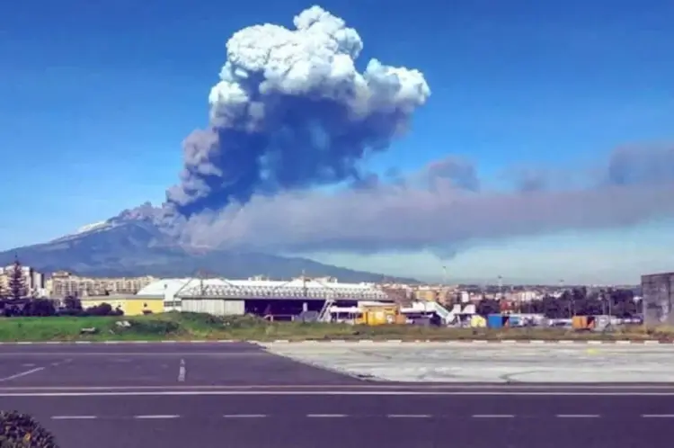 Colonna di cenere e fumo dell'Etna in eruzione vista dall'area industriale di Catania, con lo scalo aeroportuale sullo sfondo