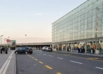 Ingresso esterno dell'aeroporto di Catania Fontanarossa con terminal in vetro, auto in sosta e passeggeri sul marciapiede.