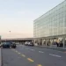 Ingresso esterno dell'aeroporto di Catania Fontanarossa con terminal in vetro, auto in sosta e passeggeri sul marciapiede.