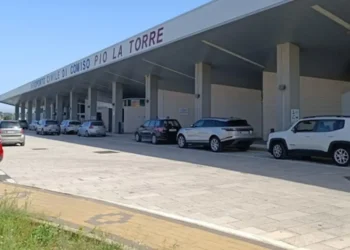 Facciata dell'aeroporto di Comiso con l'insegna Aeroporto Civile Pio La Torre e auto parcheggiate sotto la pensilina.