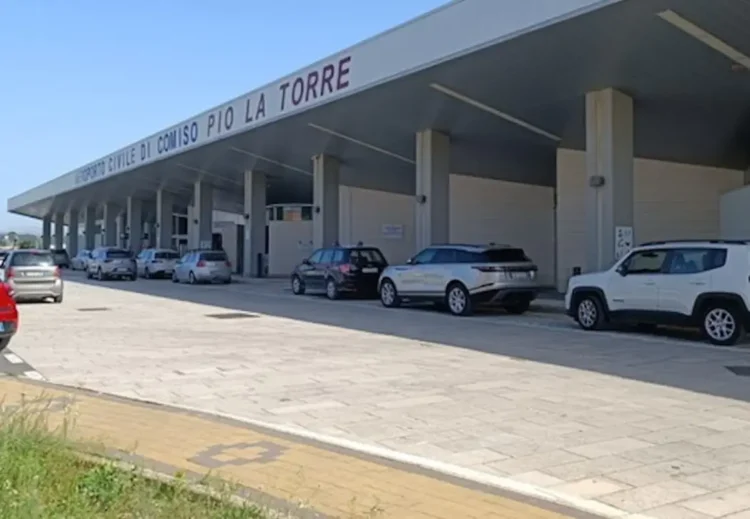Facciata dell'aeroporto di Comiso con l'insegna Aeroporto Civile Pio La Torre e auto parcheggiate sotto la pensilina.
