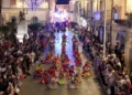 Ballerini in costume colorato si esibiscono tra la folla in una via illuminata di Chiaramonte Gulfi durante Zuppà.