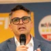 Sergio Firrincieli parla al microfono durante un evento pubblico, con manifesti elettorali sullo sfondo