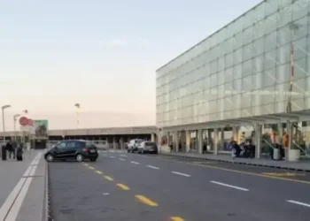 Esterno dell'aeroporto di Catania, terminal in vetro con la corsia di accesso quasi vuota e poche auto ferme