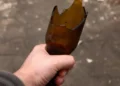Mano che stringe una bottiglia di vetro rotta, usata come arma in un'aggressione