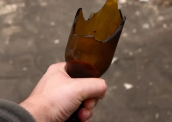 Mano che stringe una bottiglia di vetro rotta, usata come arma in un'aggressione