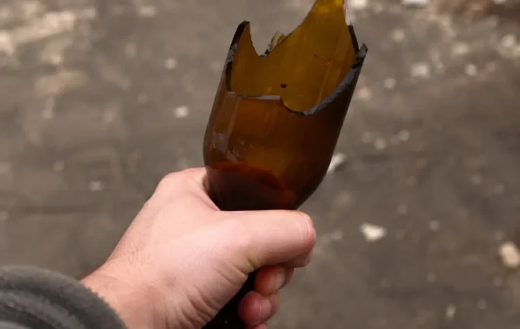 Mano che stringe una bottiglia di vetro rotta, usata come arma in un'aggressione