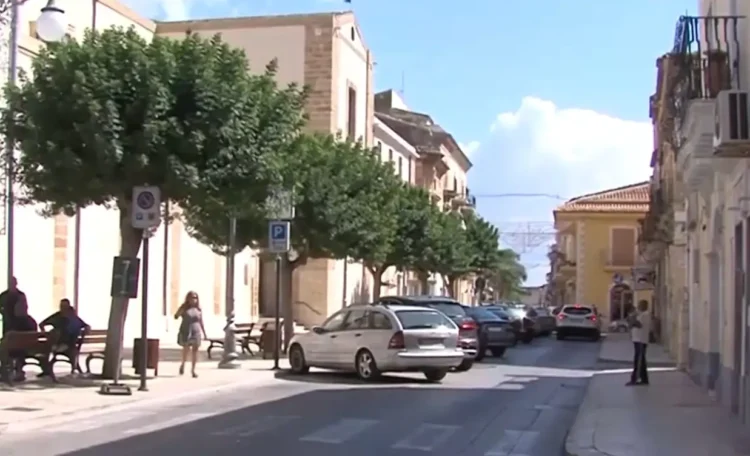 Via del centro di Santa Croce Camerina con auto parcheggiate e passanti in una giornata di sole