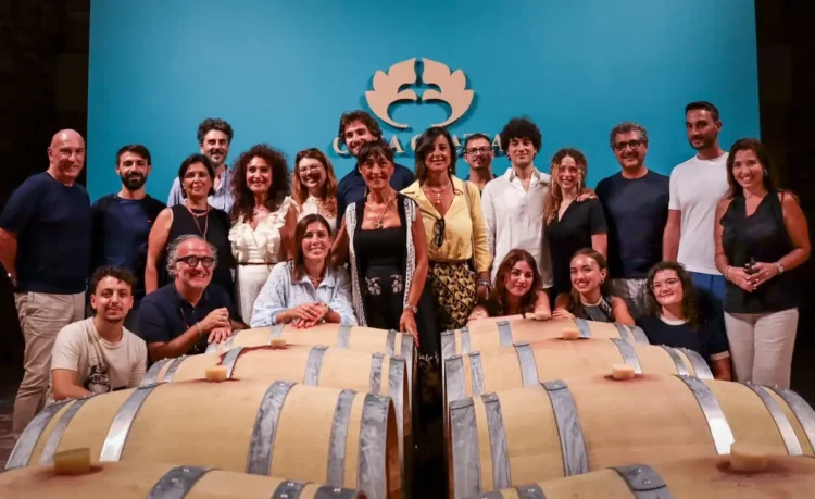 Il team di Casa Grazia posa tra le botti della cantina, sotto il logo aziendale, per la presentazione di Aischylia