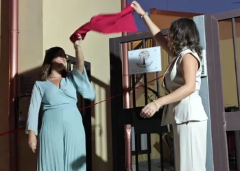 Lorena e Giusi tagliano un nastro rosso davanti all'ingresso decorato con il logo a forma di albero colorato