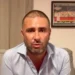 Alessandro Di Battista seduto su un divano grigio, camicia azzurra, con una cicatrice visibile sul capo rasato