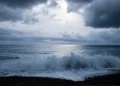 Nuvoloni scuri e mare mosso, con onde che si infrangono sulla spiaggia di ciottoli durante una fase di maltempo