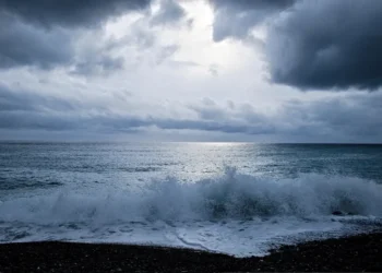 Nuvoloni scuri e mare mosso, con onde che si infrangono sulla spiaggia di ciottoli durante una fase di maltempo