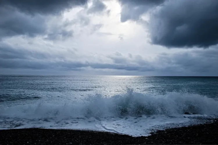 Nuvoloni scuri e mare mosso, con onde che si infrangono sulla spiaggia di ciottoli durante una fase di maltempo
