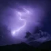 Fulmine illumina il cielo notturno durante un forte temporale, montagne in controluce sullo sfondo
