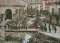 Modica dopo l'alluvione del 1902: alveo pieno di detriti tra i palazzi, gente su una passerella di legno e sulle strade