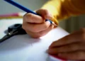 Bambino scrive con una matita blu su un foglio bianco, alle porte del nuovo anno scolastico