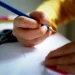 Bambino scrive con una matita blu su un foglio bianco, alle porte del nuovo anno scolastico