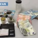 Denaro contante e materiale sequestrato dalla polizia, con una parte di un'arma visibile sul lato sinistro