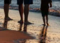 Due adulti e un bambino camminano a piedi nudi sulla battigia al tramonto