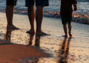 Due adulti e un bambino camminano a piedi nudi sulla battigia al tramonto