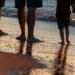 Due adulti e un bambino camminano a piedi nudi sulla battigia al tramonto