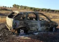 Carcassa di un'auto completamente bruciata abbandonata in un campo, con vegetazione secca intorno