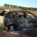 Carcassa di un'auto completamente bruciata abbandonata in un campo, con vegetazione secca intorno