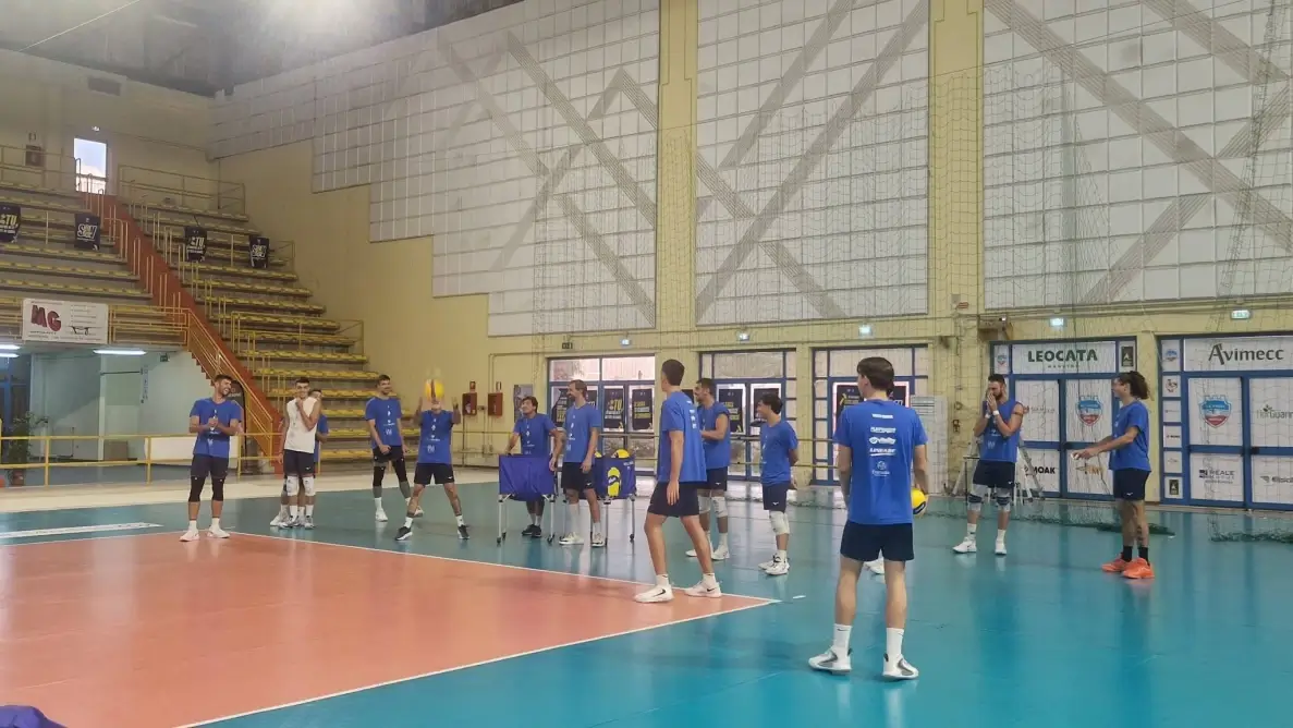 Giocatori dell'Avimec Modica in maglia blu durante un allenamento in palestra, uno palleggia al centro del campo
