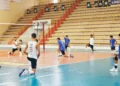 Giocatori dell'Avimec Modica si allungano a bordo campo durante il riscaldamento in palestra, spalti sullo sfondo