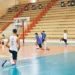 Giocatori dell'Avimec Modica si allungano a bordo campo durante il riscaldamento in palestra, spalti sullo sfondo