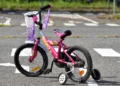 Bicicletta rosa per bambina, con rotelle e nappine, ferma su un attraversamento pedonale