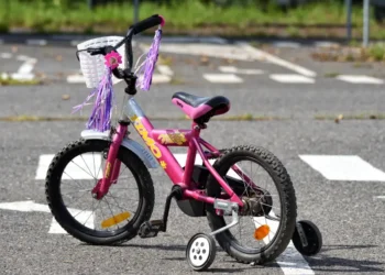 Bicicletta rosa per bambina, con rotelle e nappine, ferma su un attraversamento pedonale