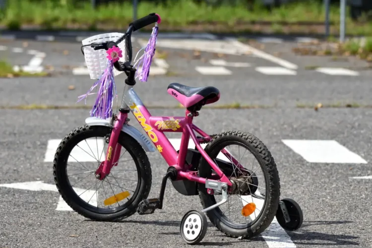 Bicicletta rosa per bambina, con rotelle e nappine, ferma su un attraversamento pedonale