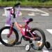 Bicicletta rosa per bambina, con rotelle e nappine, ferma su un attraversamento pedonale