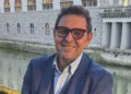 Ritratto di Gigi Bellassai, capogruppo del Pd, con occhiali e giacca blu accanto a un canale cittadino