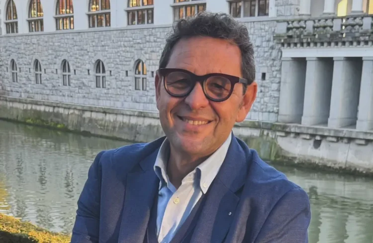 Ritratto di Gigi Bellassai, capogruppo del Pd, con occhiali e giacca blu accanto a un canale cittadino
