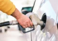 Rifornimento di carburante: mano con manica gialla tiene la pistola della pompa nel serbatoio di un'auto grigia