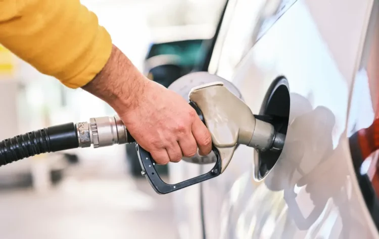 Rifornimento di carburante: mano con manica gialla tiene la pistola della pompa nel serbatoio di un'auto grigia