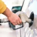 Rifornimento di carburante: mano con manica gialla tiene la pistola della pompa nel serbatoio di un'auto grigia