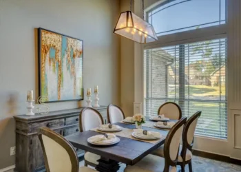 Sala da pranzo di una casa: tavolo in legno apparecchiato, lampadario e grande finestra con veneziane