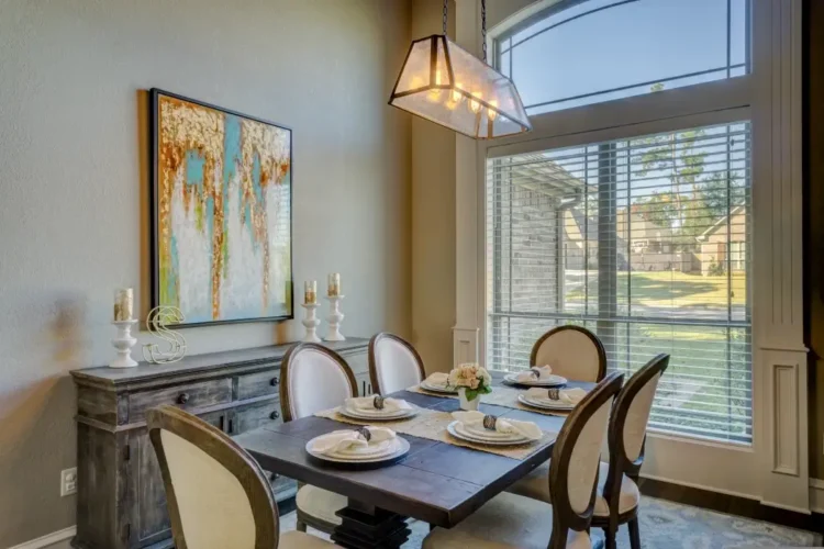 Sala da pranzo di una casa: tavolo in legno apparecchiato, lampadario e grande finestra con veneziane