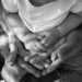 Mani di due genitori che sorreggono le mani di un bambino con la maglietta bianca, foto in bianco e nero sul tema famiglie