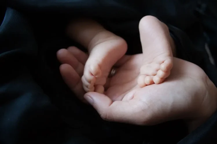 Piedini di un neonato appoggiati nel palmo della mano di un adulto, su un tessuto scuro