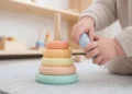 Bambino gioca con una piramide ad anelli di legno colorati su un tappeto, tra mobili in legno
