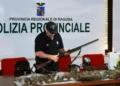 Agente della Polizia Provinciale di Ragusa esamina un fucile; sul tavolo selvaggina abbattuta e un faro portatile