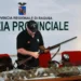 Agente della Polizia Provinciale di Ragusa esamina un fucile; sul tavolo selvaggina abbattuta e un faro portatile