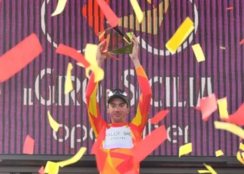 Brandon McNulty in maglia giallorossa di leader alza il trofeo sul podio del Giro di Sicilia tra coriandoli rossi e gialli