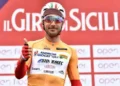Ciclista in maglia arancione del Giro di Sicilia alza il pollice davanti al pannello della corsa