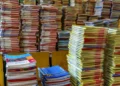 Pile di libri scolastici e quaderni con copertine colorate accatastati su banchi di legno, simili ai testi dei buoni libro